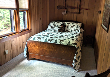 looking into the main bedroom from the hall at Cedar Cliff Cottage - windows line the lakeside, double bed, rocking chair