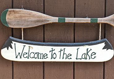 welcome to the lake sign on a canoe with a paddle on the outside wall of Cedar Cliff Cottage